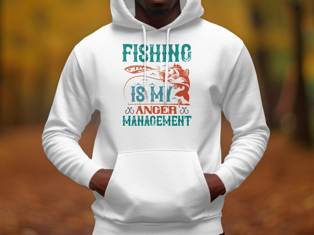A person is wearing a Garment Graphics white hoodie from the Anglers Wardrobe collection, featuring a vibrant graphic with Fishing is my anger management and a fish caught by a rod, standing amid blurred autumn foliage.