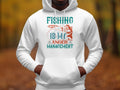 A person is wearing a Garment Graphics white hoodie from the Anglers Wardrobe collection, featuring a vibrant graphic with Fishing is my anger management and a fish caught by a rod, standing amid blurred autumn foliage.