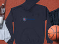 A black Garment Graphics hoodie featuring Scania’s iconic logo and blue text lies on a textured surface next to a clear water bottle, white towel, black athletic shorts, and a basketball, combining sporty style with uniqueness.