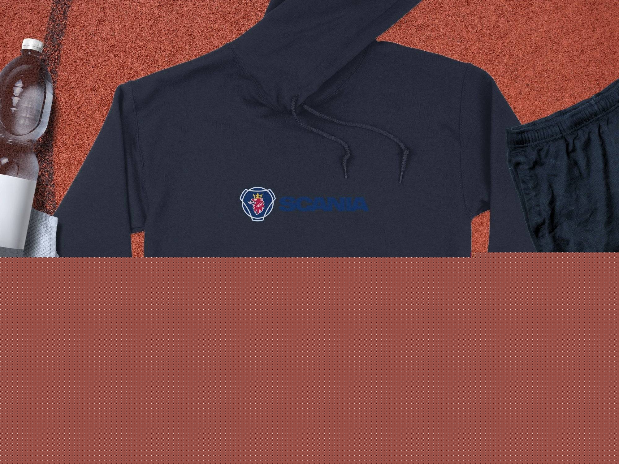 A black Garment Graphics hoodie featuring Scania’s iconic logo and blue text lies on a textured surface next to a clear water bottle, white towel, black athletic shorts, and a basketball, combining sporty style with uniqueness.