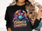 Sporting an urban style, a person wears a black sweatshirt by Garment Graphics with a gorilla illustration dressed as a gangster. Complete with sunglasses, hat, gold chain, and cigar, the ape exudes Gorilla Gangster vibes. The bold text GORILLA GANGSTER appears below the image.