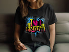 A person is lounging on a couch wearing Garment Graphics black T-shirt featuring a vibrant street art design with I Love Graffiti in bold, complete with blue splashes, yellow blocks, and a cracked pink heart.