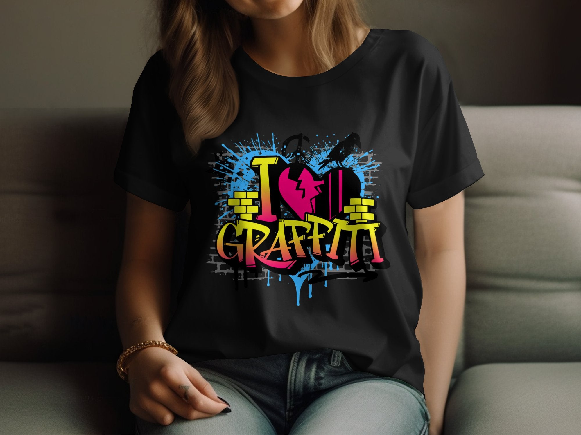 A person is lounging on a couch wearing Garment Graphics black T-shirt featuring a vibrant street art design with I Love Graffiti in bold, complete with blue splashes, yellow blocks, and a cracked pink heart.