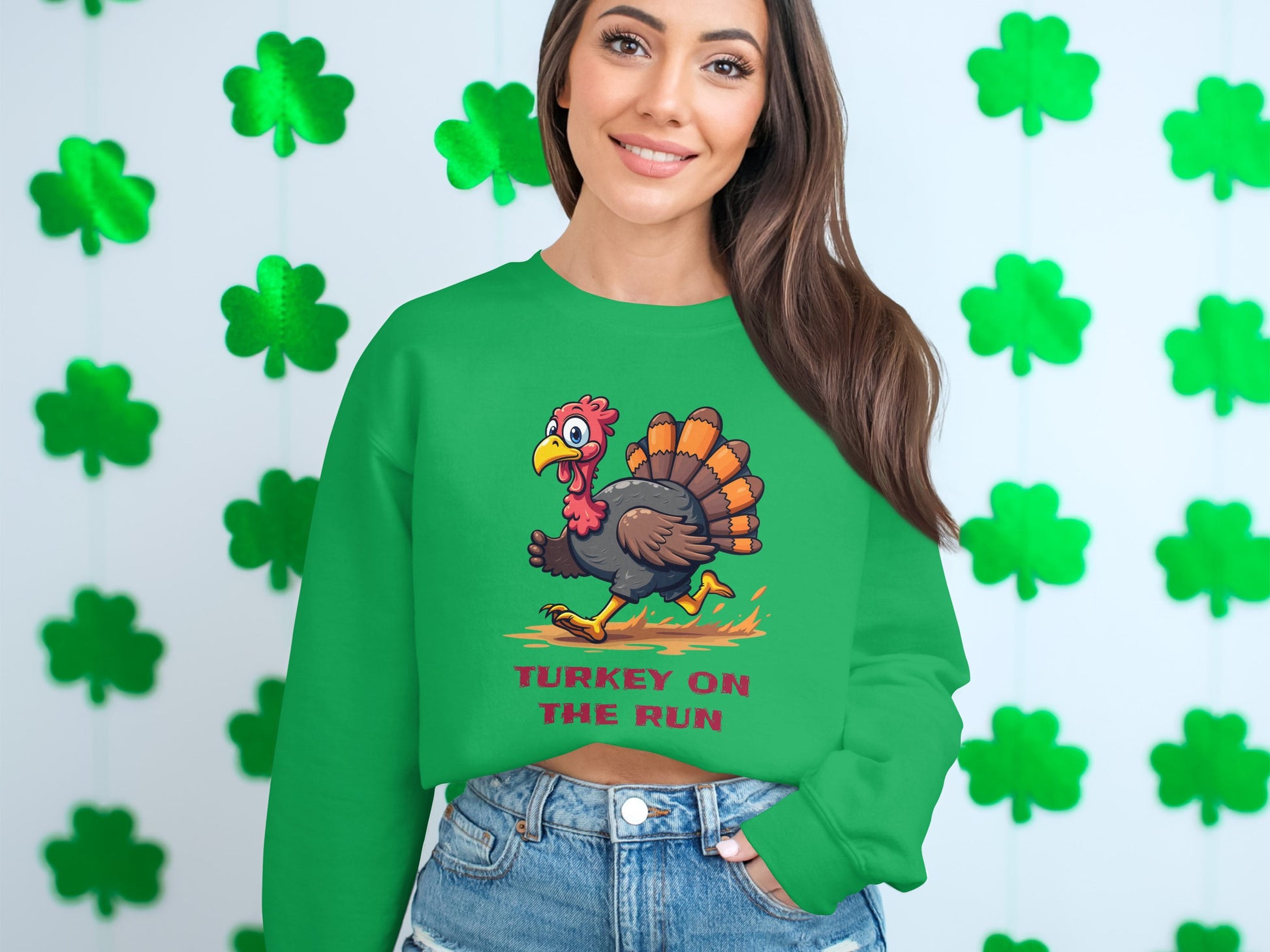 Someone in a Garment Graphics green sweatshirt featuring a cartoon turkey and Turkey on the Run enjoys this humorous design from their collection. With green shamrocks on a white wall background, theyre in denim shorts, showcasing its unisex appeal.