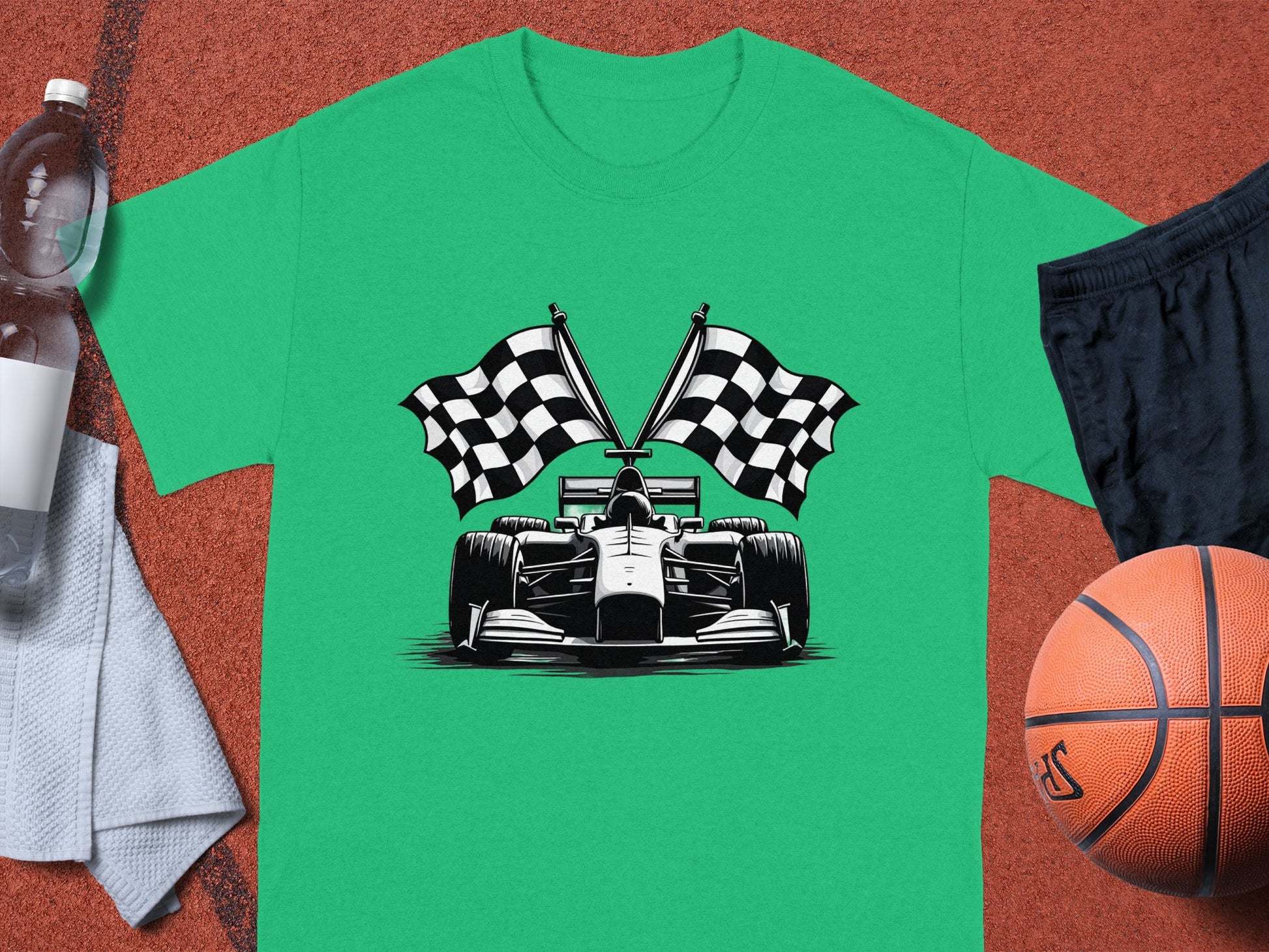 A Garment Graphics green graphic T-shirt with a racing car and crossed checkered flags lies on a court, surrounded by essentials: a water bottle, towel, black shorts, and a basketball—a perfect tribute to the excitement of motorsport.