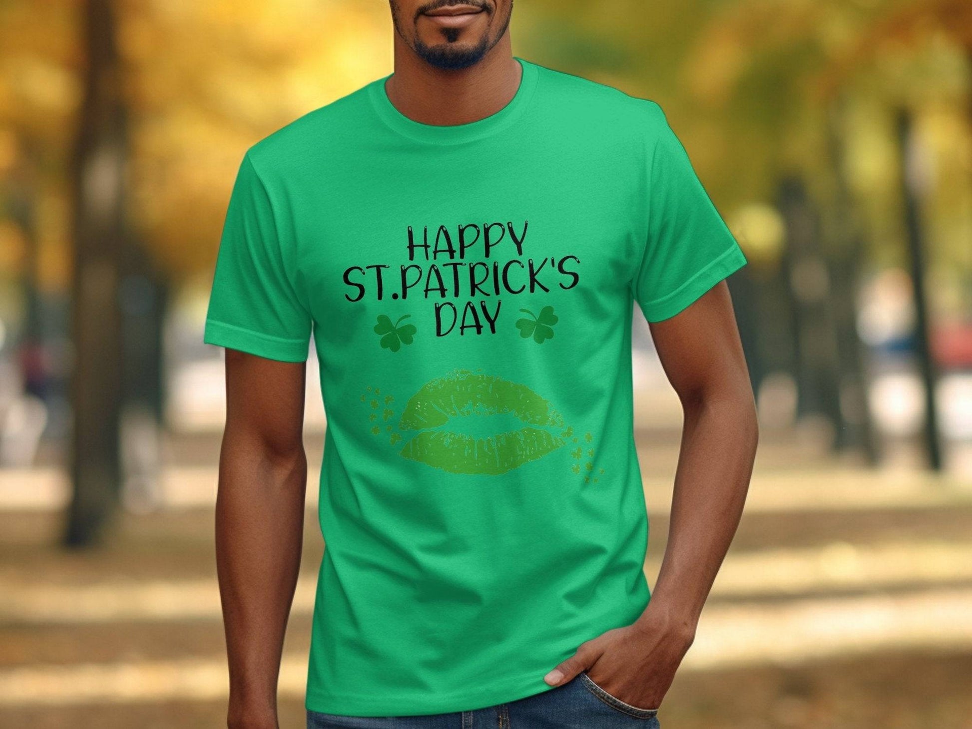A person wears a Garment Graphics T-shirt featuring Happy St. Patricks Day text, green lips, and clovers. In the background, theres a tree-lined path with vibrant green and yellow leaves.