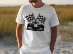 A man wearing a Garment Graphics T-shirt featuring a race car and crossed checkered flags stands outdoors in a grassy landscape, embodying the excitement of motorsport.