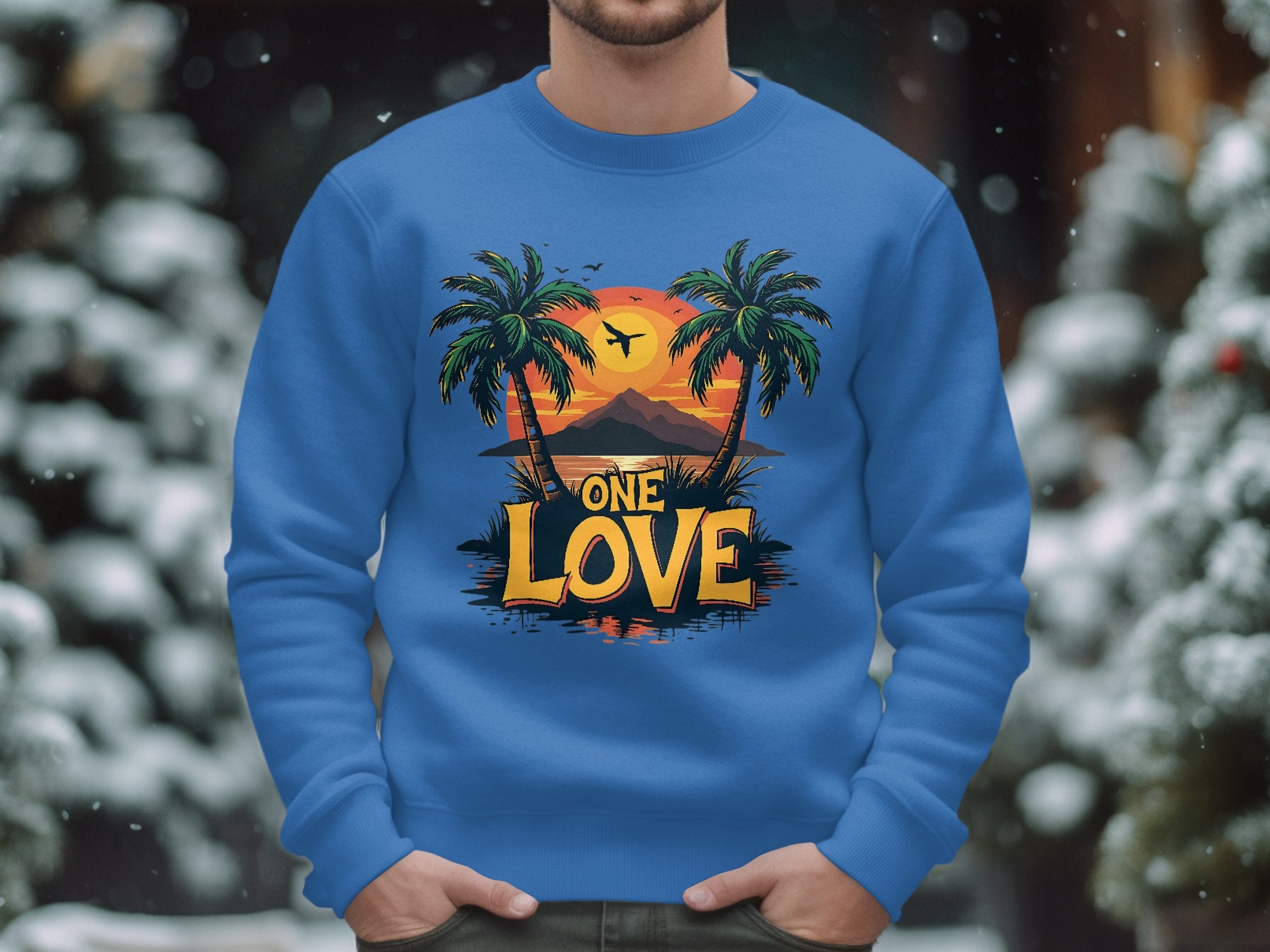 Garment Graphics offers a unisex blue One Love Sweatshirt featuring a tropical sunset with palm trees, a plane, and mountains. The words One Love stand out boldly as snow-covered trees blur in the background.