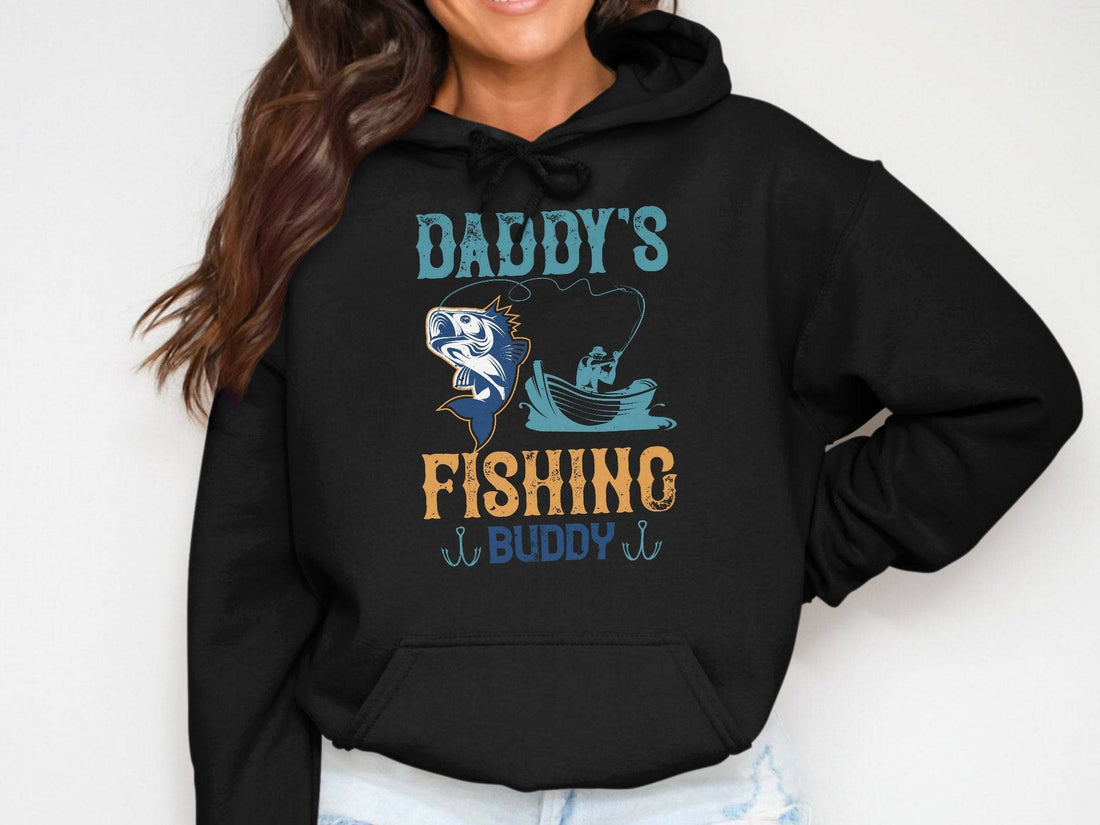 Someone wearing a Garment Graphics black graphic hoodie featuring Daddys Fishing Buddy with a fish and boat design stands with hands in pockets, ready for outdoor adventures.