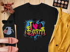 A black sweatshirt from Garment Graphics featuring I love graffiti in vibrant design rests on wood, encircled by sunglasses, makeup brushes, a palette, a yellow jacket, pink shoes, and a blue pouch—ideal for an urban style enthusiast.
