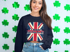 Wearing a navy Garment Graphics sweatshirt with the Union Jack and Dont Blame Me, I Didnt Vote For Him, a person stands against a backdrop with green shamrock decorations. This stylish unisex piece suits any wardrobe.