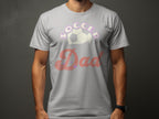 A person wearing a Garment Graphics T-shirt against a dark background sports Soccer Dad with Soccer in vivid purple above a soccer ball and Dad in bold red adorned with stars.