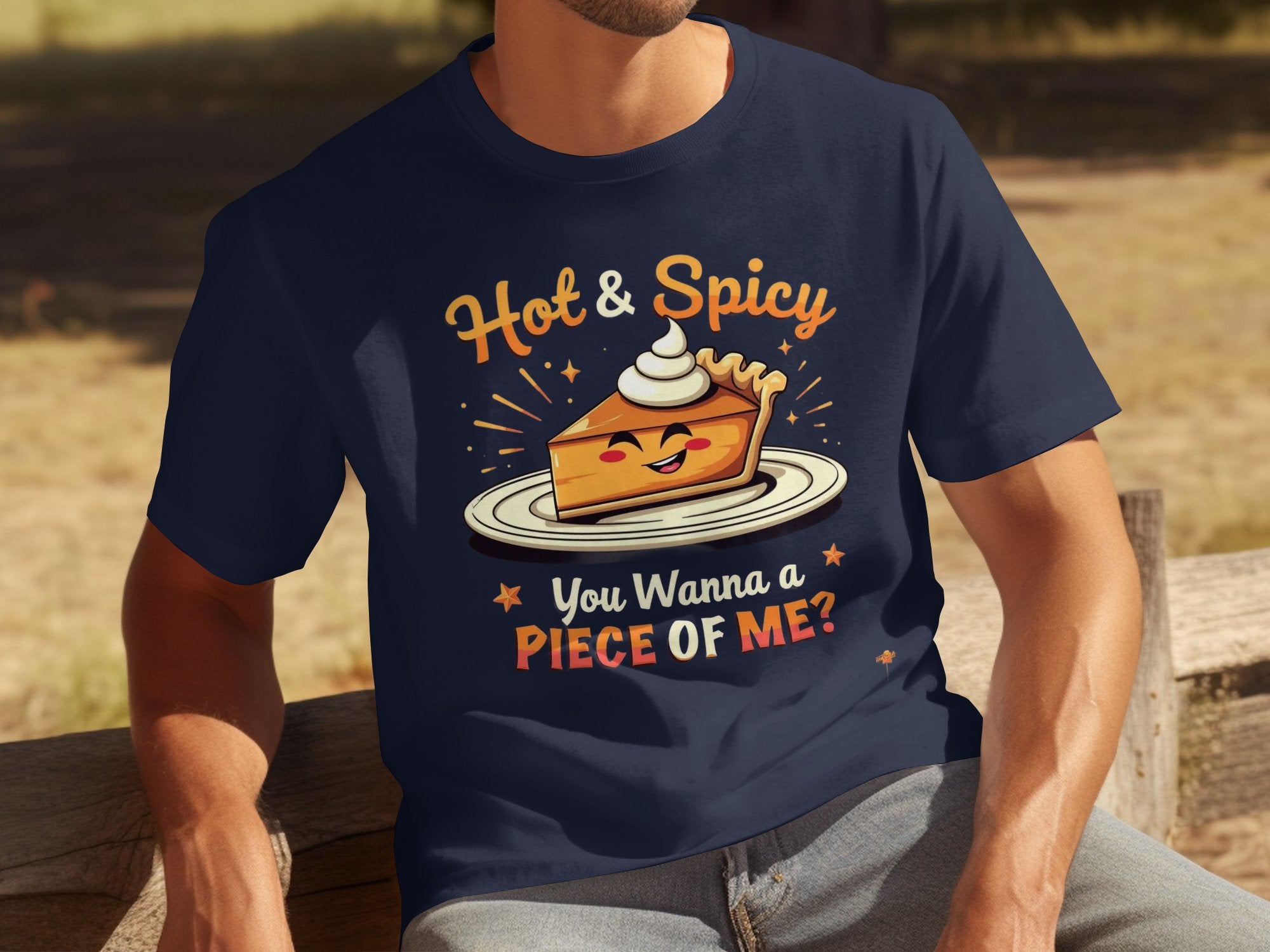 A person sits on a bench, wearing a navy t-shirt from Garment Graphics with the Hot and Spicy Pie Design. The shirt features a cheeky pie slice with whipped cream and the bold text, You Wanna a Piece of Me? Dappled sunlight partially obscures them as they relax outdoors.
