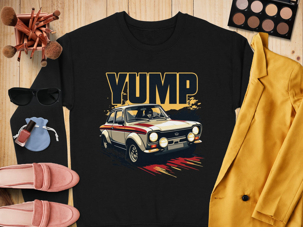 A black YUMP design rally car graphic T-shirt by Garment Graphics is on a wooden surface. Nearby are a yellow blazer, sunglasses, makeup palette with brushes, pink shoes, lip products, and a blue pouch. Ideal for pairing with trendy sweatshirts for casual outings.