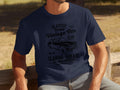 Sporting a Garment Graphics navy blue T-shirt with retro automotive graphics, including Classic London City Vintage Car Club and Classic Garage Old School Automotive, this person exudes timeless style in a classic fit tee while sitting on a wooden bench outdoors.