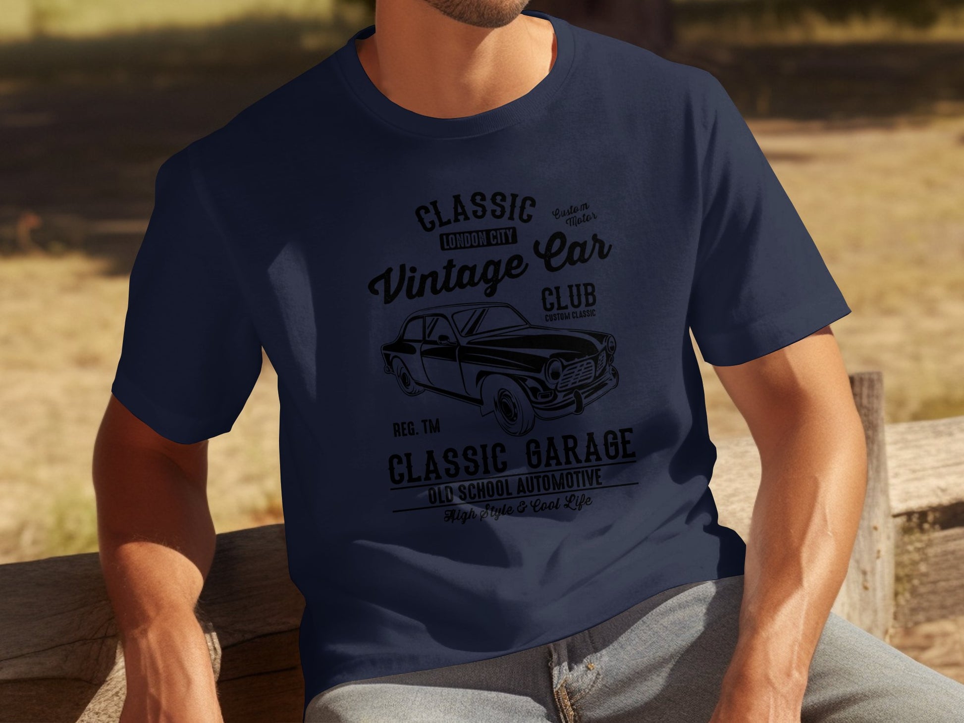 Sporting a Garment Graphics navy blue T-shirt with retro automotive graphics, including Classic London City Vintage Car Club and Classic Garage Old School Automotive, this person exudes timeless style in a classic fit tee while sitting on a wooden bench outdoors.