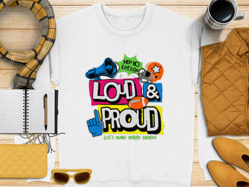 Garment Graphics white unisex t-shirt showcases a colorful graphic of a megaphone, football, and foam finger with Hey Ho Lets Go Loud & Proud Lets Make Some Noise! text design. Its styled alongside a scarf, coffee, notebook, pen, jacket, wallet, and sunglasses on wood.