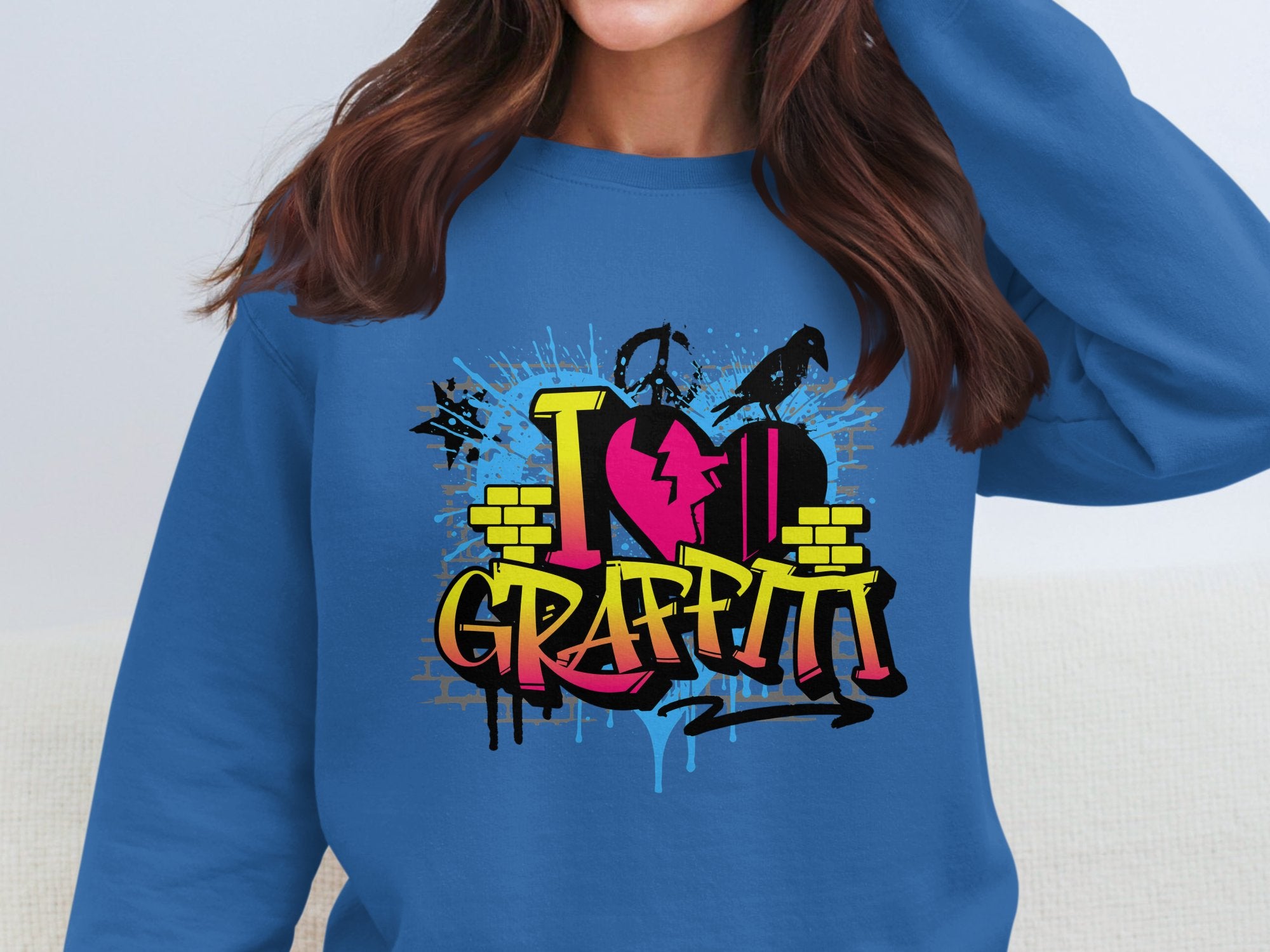 A person wears a Garment Graphics sweatshirt showcasing urban-style graffiti with bold I ♥ GRAFFITI text, spray cans, and paint splatters. Their face is not visible.