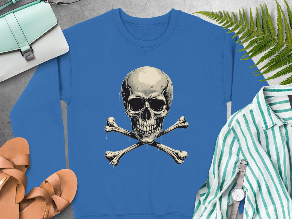 Garment Graphics offers a blue sweatshirt with a skull and crossbones graphic for an edgy look. It pairs well with a mint handbag, tan sandals, striped shirt, wristwatch, and fern leaf on a light gray surface. Unisex sizing ensures versatile wear for all styles.