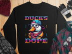 Garment Graphics offers a trendy black sweatshirt with a cartoon duck wearing glasses, a hat, and scarf, and the bold phrase Ducks Dope in vibrant text. The design is displayed on a wooden surface, accompanied by winter accessories.