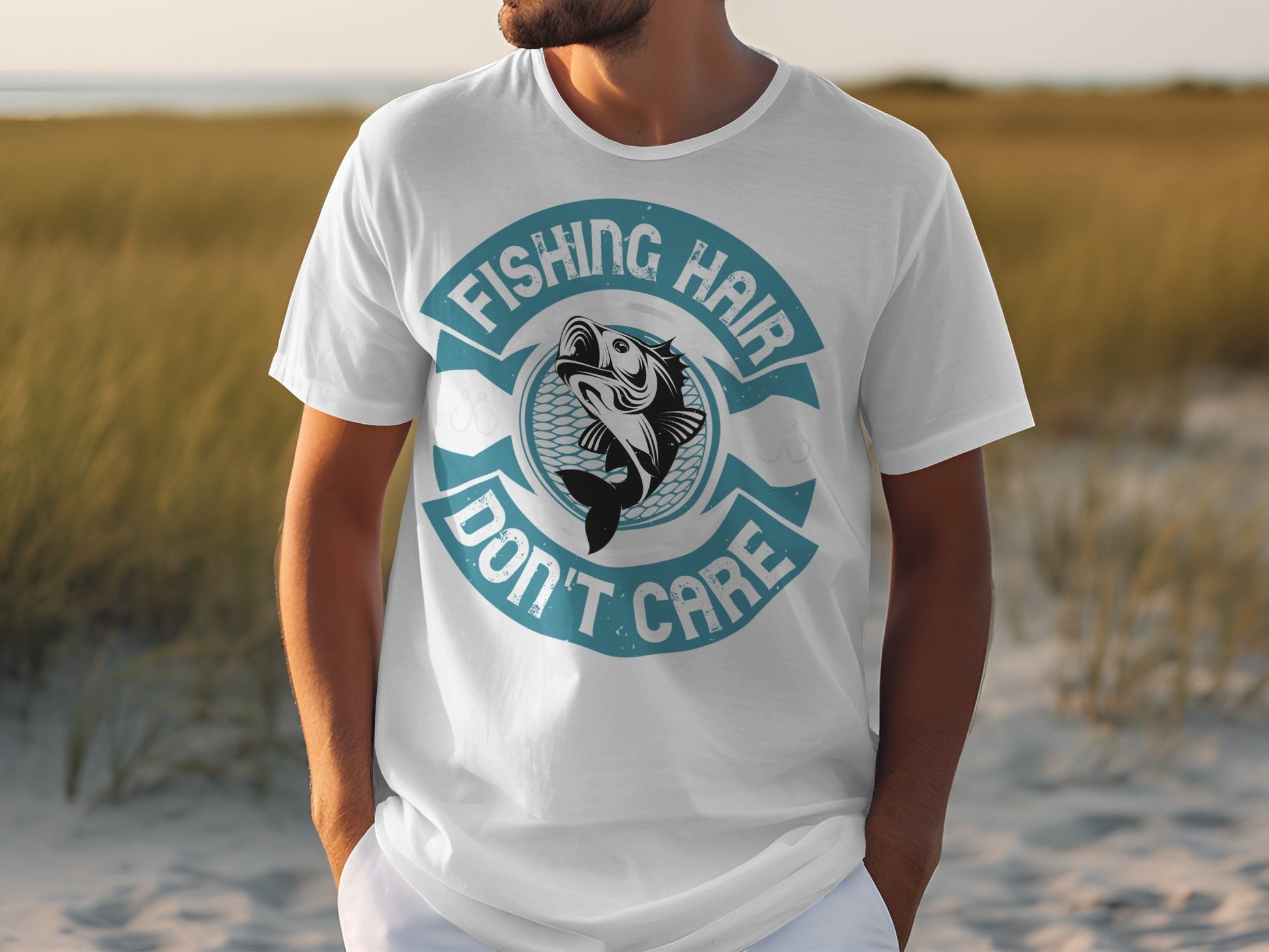 Amid grassy dunes and a cloudy sky, a person wears a white graphic tee by Garment Graphics, featuring a fish and the design Fishing Hair Dont Care.